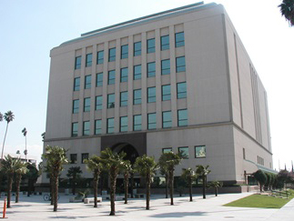 Riverside Hall of Justice framed by manicured trees and bushes beneath a clear blue sky.